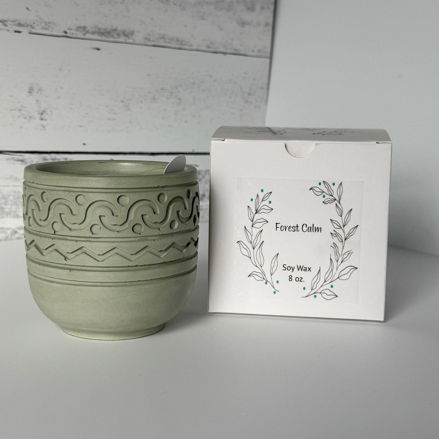 Forest Calm Candle in a moss colored concrete jar with packaging in the background